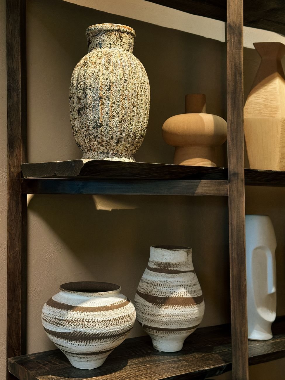 Artisan ceramic vases displayed on rustic wooden shelves, warm natural tones.
