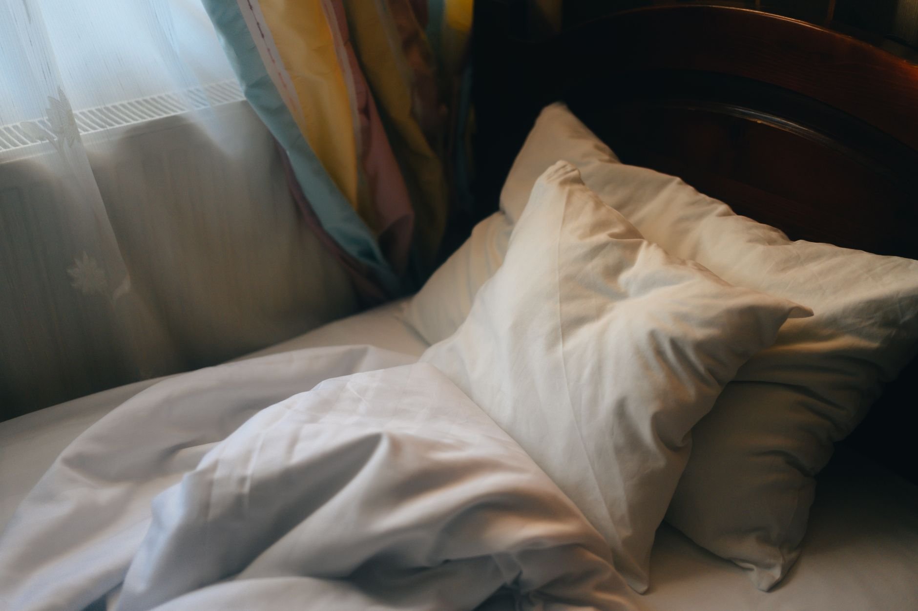 Inviting unmade bed with soft pillows in morning light, creating a cozy atmosphere.